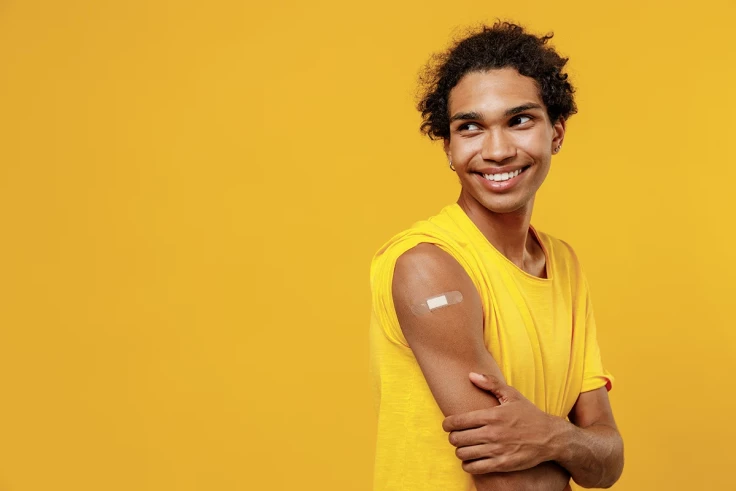 A young person post vaccination with plaster on arm on yellow background